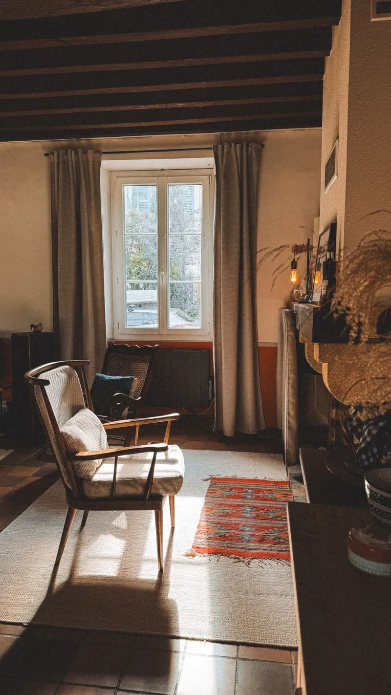 Sunlit room with plaster walls, a wooden chair and warm wood beams